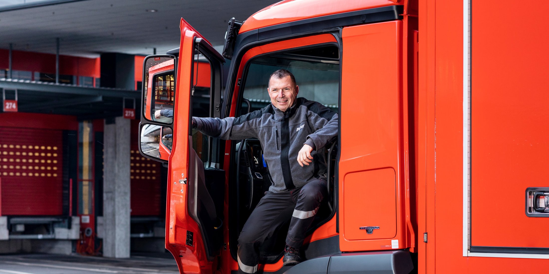 Lachender Pistor LKW-Fahrer mit offener Tür im LKW-Cockpit